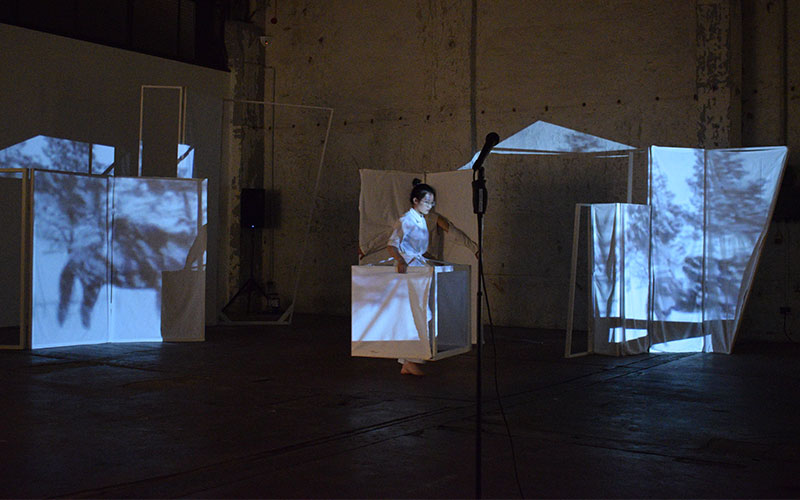 Performer Wei Zhang is walking with a set element while projection is mapped on top of that element